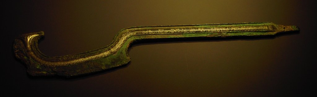 A photograph of an ancient Bronze Age khopesh sword — a curved, sickle‑shaped blade made of bronze with electrum inlays, found near Nablus (Shechem) and now in a museum collection, illustrating the characteristic weapon design used in the Near East during the Middle Bronze Age.
