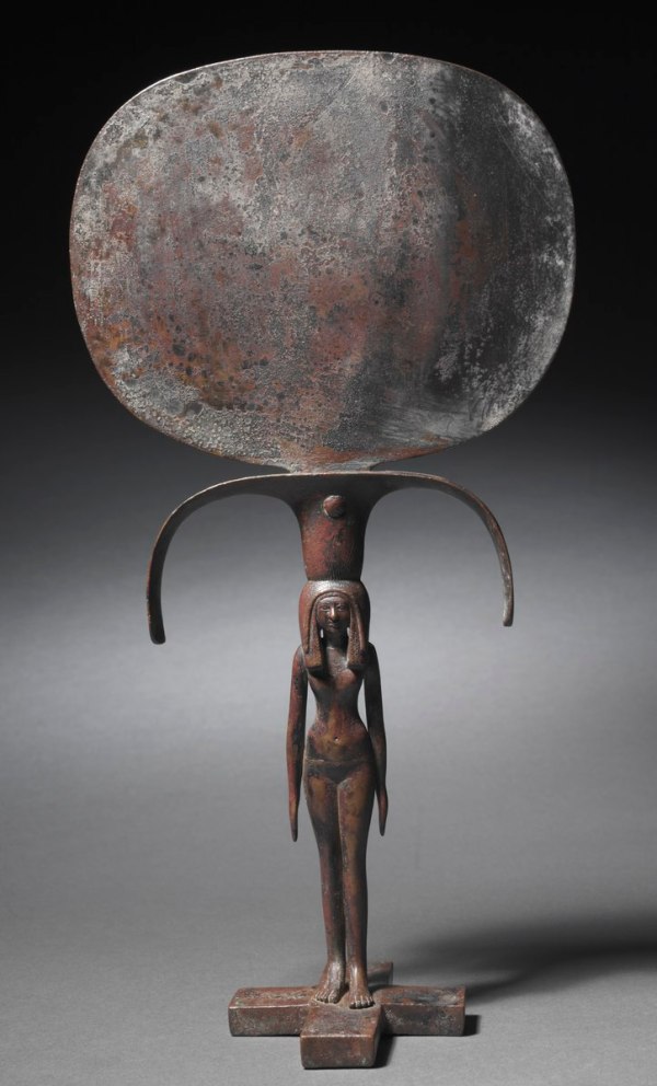 Bronze caryatid mirror from Egypt’s New Kingdom (Dynasty 18) — a hand mirror with an oval bronze reflective disk and a handle in the form of a young woman supporting it, an example of finely crafted ancient Egyptian metalwork.