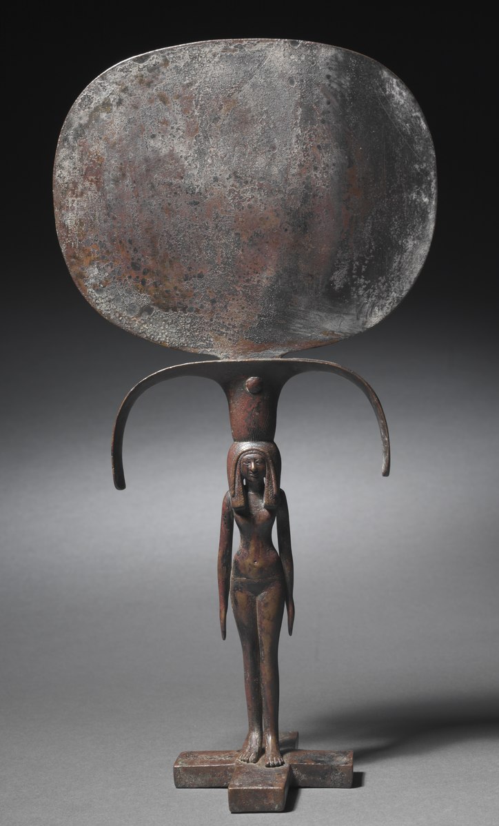 Bronze caryatid mirror from Egypt’s New Kingdom (Dynasty 18) — a hand mirror with an oval bronze reflective disk and a handle in the form of a young woman supporting it, an example of finely crafted ancient Egyptian metalwork.