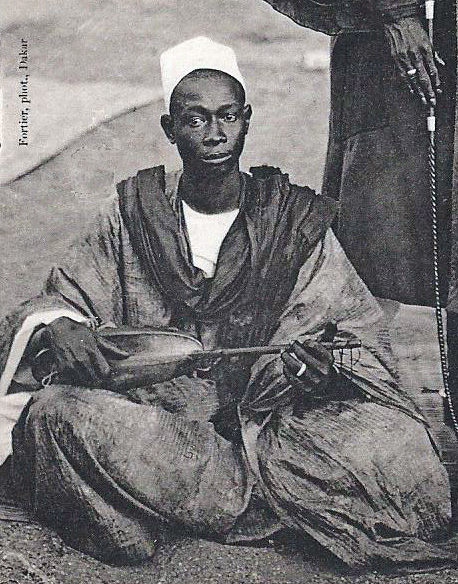 Photograph of a West African chief standing with his griot, the traditional oral historian and genealogist, both in ceremonial dress.