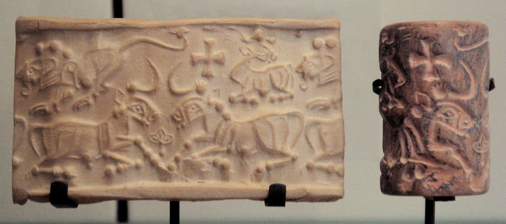 Photo of a small ancient Proto-Elamite cylinder seal (circa 3150–2800 BC) showing carved figures and symbols on stone, displayed on a stand at the Louvre Museum.