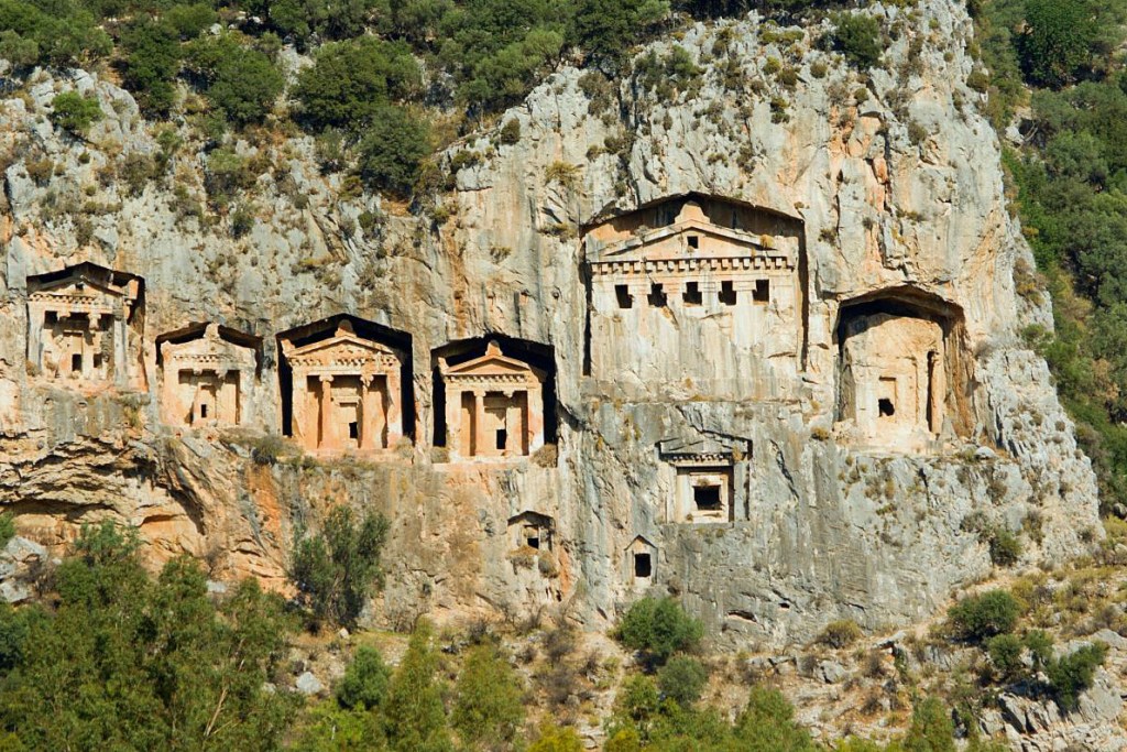 Photograph of ancient Lycian rock‑cut tombs near Dalyan, Turkey, carved into the cliff face overlooking the river and town, illustrating the monumental burial practices of the ancient Lycian people.